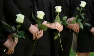 Ludzie w czerni trzymają białe róże. Mogą symbolizować żałobę, ale też nadzieję, która bywa trudna dla osób wierzących, gdy pojawiają się przyczyny lęku przed śmiercią.