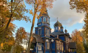 Niebieska cerkiew na Podlasiu, z kopułami i krzyżami, w jesiennym otoczeniu. Jak rozpoznać architekturę sakralną różnych wyznań na Podlasiu?