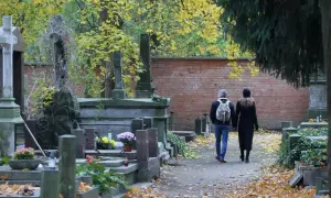 Jesienne zaduszki na cmentarzu. Para spaceruje alejką wśród nagrobków. Jak zabezpieczyć wiązanki i znicze przed kradzieżą?