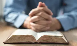 Modlące się dłonie nad otwartą Biblią. Warto zastanowić się, jak rozpoznać prawdziwe powołanie do kapłaństwa lub zakonu.