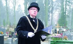 Mistrz ceremonii w czarnym stroju i z łańcuchem na szyi prowadzi pogrzeb świecki, podkreślając różnicę między nim a wyznaniowym.