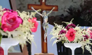 Drewniany krzyż z figurą Chrystusa, otoczony bukietami róż i białych kwiatów. Czy zdrada w myślach grzech?