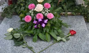 Wieniec z różowych i białych kwiatów, zieleni i fioletowej wstążki na nagrobku.