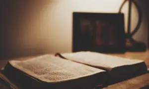Otwarta Biblia na stole, obok ramka ze zdjęciem. Czy granie w lotto to grzech? Szukamy odpowiedzi w Piśmie Świętym.