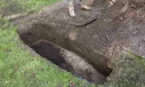 Otwarty grób z widoczną trumną i osobą kopiącą łopatą.