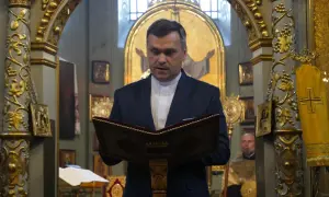 Duchowny w kościele polskokatolickim czyta z księgi. Wnętrze świątyni zdobią złote ornamenty i ikony.