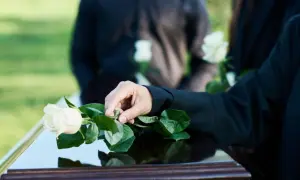 Dłoń kładzie białą różę na trumnie. Czy zmarły widzi swój pogrzeb?