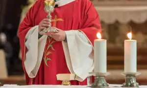 Kapłan w czerwonej szacie z kielichem, świece i patena. To fragment uroczystości, która może być częścią konsekracji kościoła.