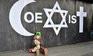 Dziecko z pluszakiem pod symbolem "COEXIST" na tle ścian, ilustrujące skutki nadmiernego intelektualizowania wiary kosztem doświadczenia.