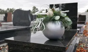 Srebrna doniczka z zimową dekoracją na nagrobku, wśród innych pomników.