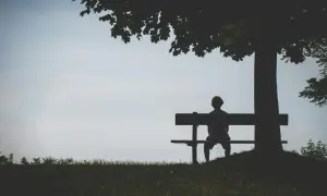 Samotna postać na ławce pod drzewem. Obraz symbolizuje skutki izolacji religijnej dla rozwoju osobistego i społecznego, pokazując samotność i wycofanie.