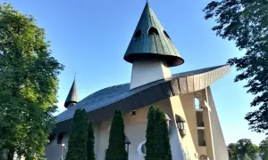 Nowoczesne sanktuarium z zielonymi dachami i krzyżem na szczycie, otoczone drzewami.