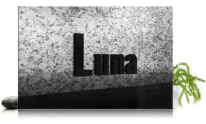 Czarna tablica z napisem "Luna" na tle granitu, z kamieniem i rośliną.
