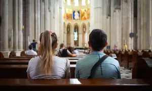 Para siedzi w kościele, zastanawiając się, czy katolik to chrześcijanin. Wnętrze świątyni z witrażami i kolumnami.