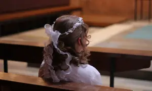 Jak rozmawiać z dziećmi o bogu i kościele porady pedagogów. Dziewczynka w białej sukience i wianku na głowie siedzi w kościele.