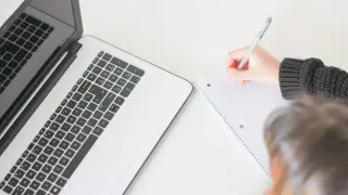 Osoba pisze w notatniku obok laptopa. Jak praktykować wiarę w miejscu pracy zachowując profesjonalizm, to temat refleksji.
