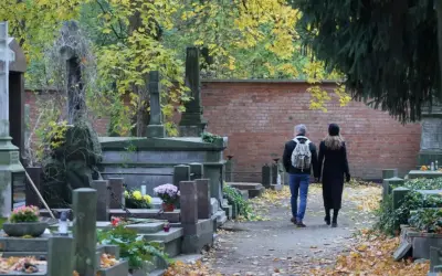 Jesienne zaduszki na cmentarzu. Para spaceruje alejką wśród nagrobków. Jak zabezpieczyć wiązanki i znicze przed kradzieżą?