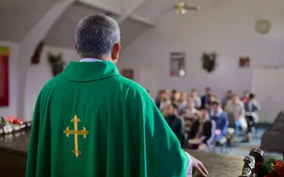 Ksiądz w zielonej szacie z krzyżem, przed wiernymi. Rozważania o skutkach ekskomuniki, czym jest i kogo może dotyczyć.