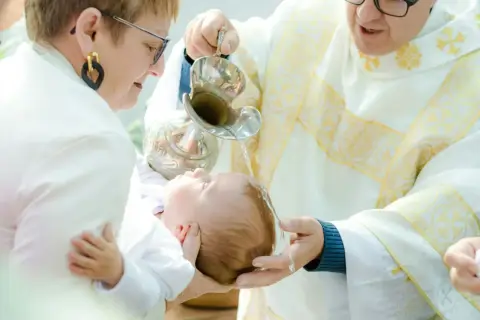 Chrzciny to wzruszająca uroczystość. Kapłan polewa wodą głowę dziecka, a rodzice trzymają je czule.