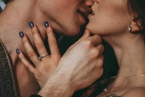 Zbliżenie na usta pary całującej się, dłoń z pierścionkiem i paznokciami.