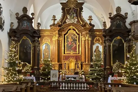 Ołtarz główny kościoła z obrazem Matki Boskiej, ozdobiony choinkami i iluminacjami.