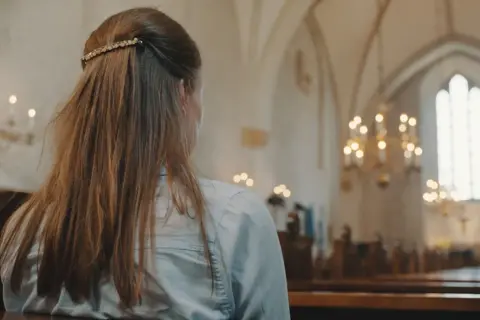 Młoda kobieta w kościele, rozważająca przyczyny utraty wiary u młodzieży. Wyniki badań socjologicznych 2026.