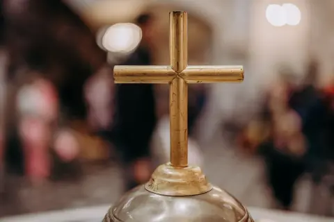 Złoty krzyż na ołtarzu, symbol wiary i 5 przykazań kościelnych. W tle rozmyte postacie wiernych.