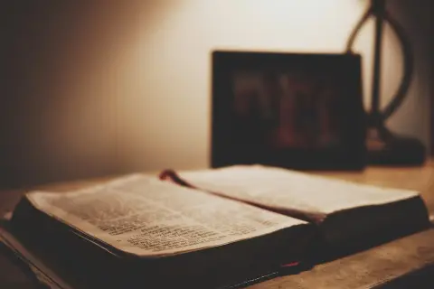 Otwarta Biblia na stole, obok ramka ze zdjęciem. Czy granie w lotto to grzech? Szukamy odpowiedzi w Piśmie Świętym.