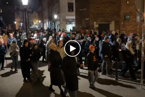 Tłum ludzi idzie ulicą nocą, trzymając świece. To uroczysta chwila, kiedy jest droga krzyżowa.