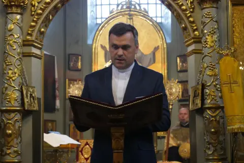 Duchowny w kościele polskokatolickim czyta z księgi. Wnętrze świątyni zdobią złote ornamenty i ikony.