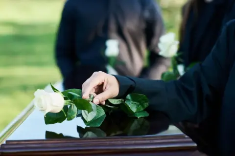 Dłoń kładzie białą różę na trumnie. Czy zmarły widzi swój pogrzeb?