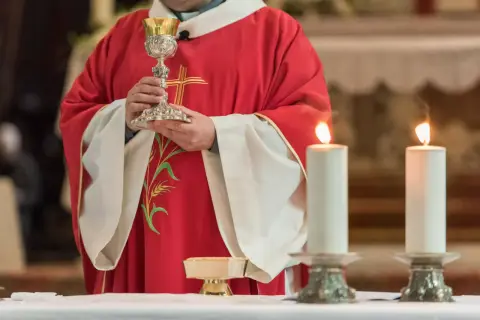Kapłan w czerwonej szacie z kielichem, świece i patena. To fragment uroczystości, która może być częścią konsekracji kościoła.