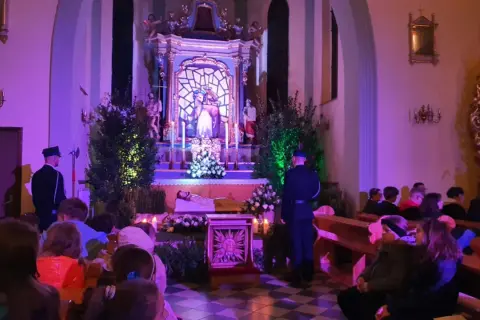 Wnętrze bazyliki Grobu Pańskiego, przygotowania do nocnej modlitwy. Wierni siedzą w ławkach, przy ołtarzu stoi wartownik.
