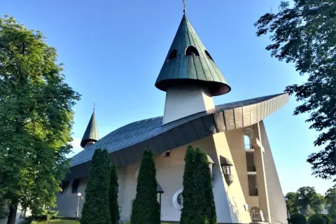 Nowoczesne sanktuarium z zielonymi dachami i krzyżem na szczycie, otoczone drzewami.