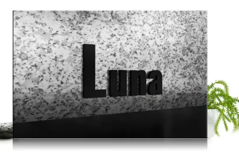 Czarna tablica z napisem "Luna" na tle granitu, z kamieniem i rośliną.