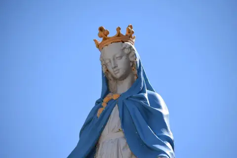 Posąg Matki Boskiej w koronie na tle błękitnego nieba.
