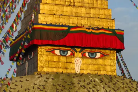 Złota stupa z oczami Buddy, ozdobiona kolorowymi flagami modlitewnymi. Warto odwiedzić takie miejsca święte w buddyzmie w Nepalu i Indiach.