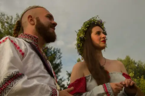 Para młoda w tradycyjnych strojach, symbolizująca żywą wiarę i tradycję przekazywaną w rodzinie.
