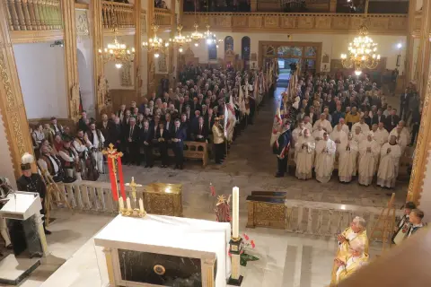 W kościele trwa litania do wszystkich świętych. Wierni i duchowni zgromadzeni na nabożeństwie, wśród nich osoby w strojach regionalnych.