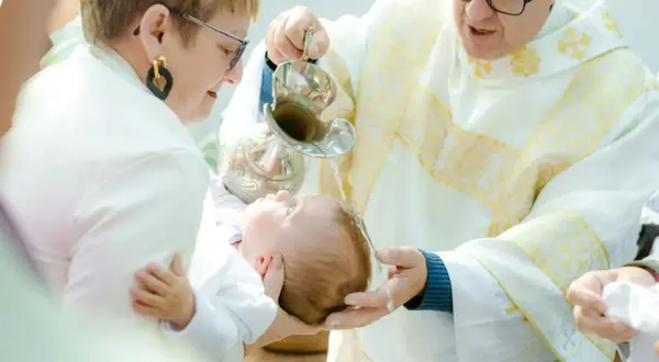 Chrzciny to wzruszająca uroczystość. Kapłan polewa wodą głowę dziecka, a rodzice trzymają je czule.
