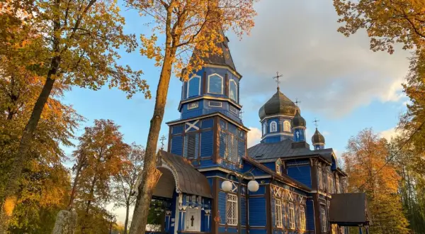 Niebieska cerkiew na Podlasiu, z kopułami i krzyżami, w jesiennym otoczeniu. Jak rozpoznać architekturę sakralną różnych wyznań na Podlasiu?
