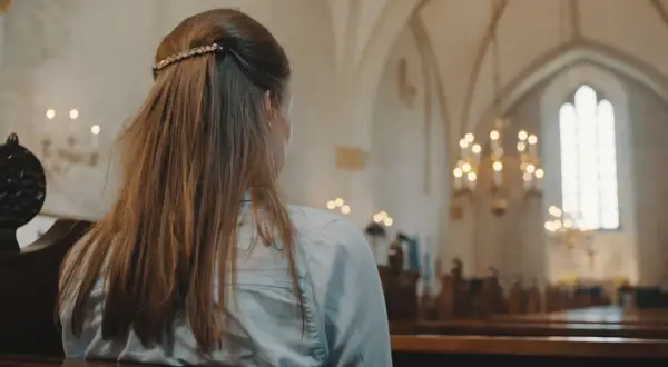 Młoda kobieta w kościele, rozważająca przyczyny utraty wiary u młodzieży. Wyniki badań socjologicznych 2026.