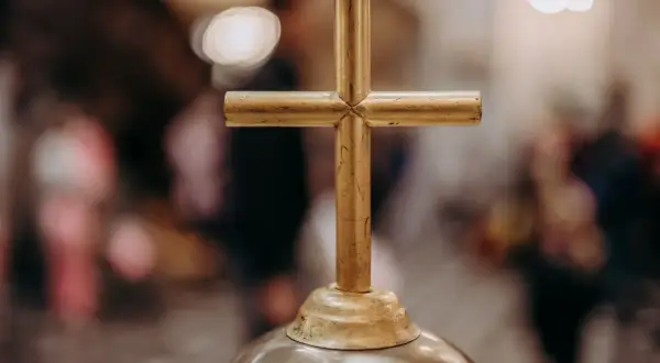 Złoty krzyż na ołtarzu, symbol wiary i 5 przykazań kościelnych. W tle rozmyte postacie wiernych.