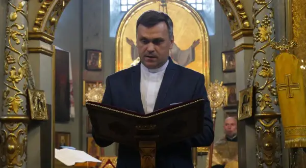 Duchowny w kościele polskokatolickim czyta z księgi. Wnętrze świątyni zdobią złote ornamenty i ikony.