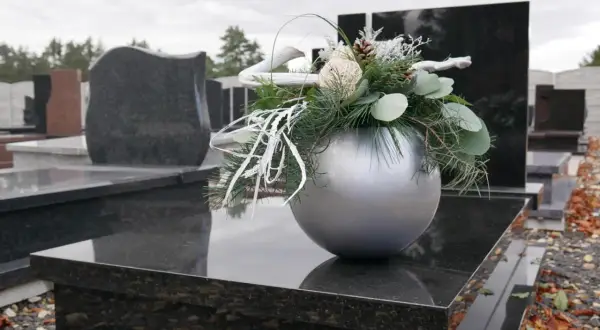 Srebrna doniczka z zimową dekoracją na nagrobku, wśród innych pomników.