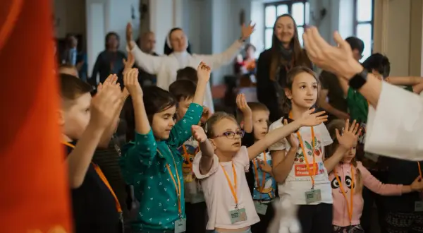 Dzieci z podniesionymi rękami, pytają, czy warto jechać na rekolekcje w milczeniu dla pogłębienia wiary.