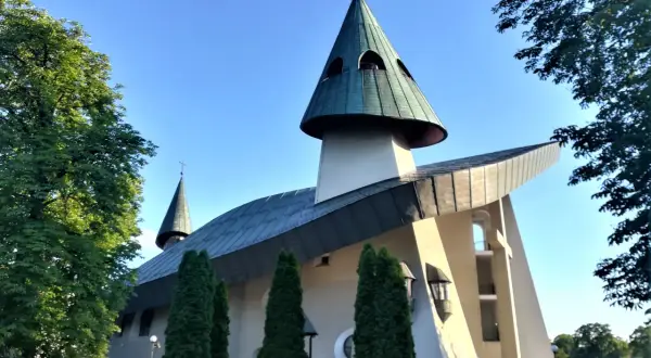 Nowoczesne sanktuarium z zielonymi dachami i krzyżem na szczycie, otoczone drzewami.