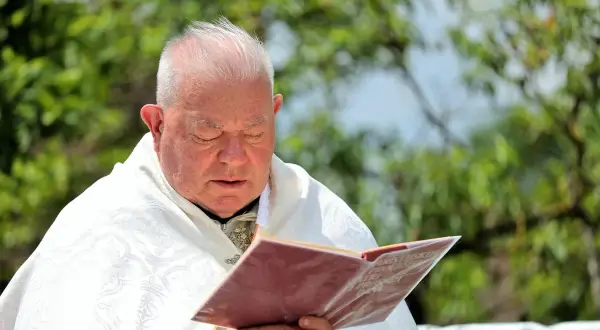 Duchowny w białej szacie czyta księgę. Zastanawia się, czy prezerwatywa to grzech, szukając odpowiedzi w świętych tekstach.
