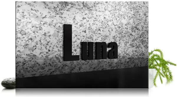 Czarna tablica z napisem "Luna" na tle granitu, z kamieniem i rośliną.