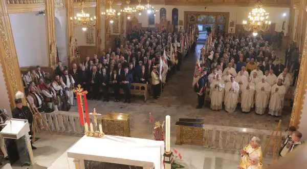 W kościele trwa litania do wszystkich świętych. Wierni i duchowni zgromadzeni na nabożeństwie, wśród nich osoby w strojach regionalnych.